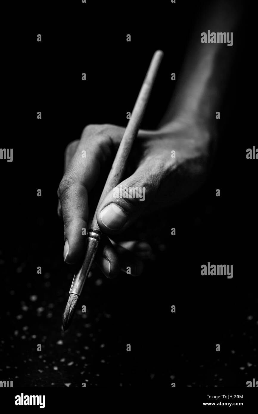 The artist's hands hold a brush. On a black background with deep shadows and bright highlights. Black and white conceptual image Stock Photo