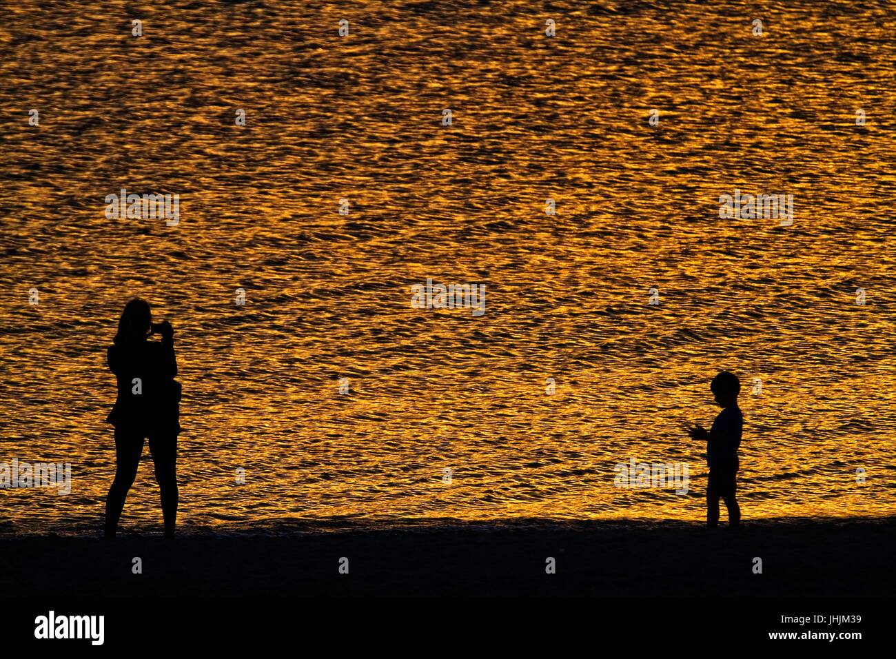 Golden sunset. Seaside. Silhouettes of mother and child. Stock Photo