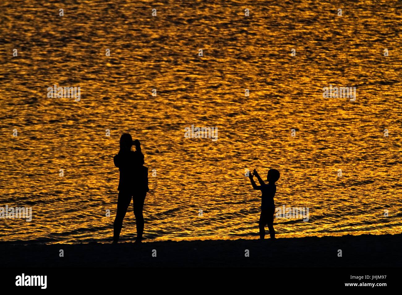 Golden sunset. Seaside. Silhouettes of mother and child. Stock Photo