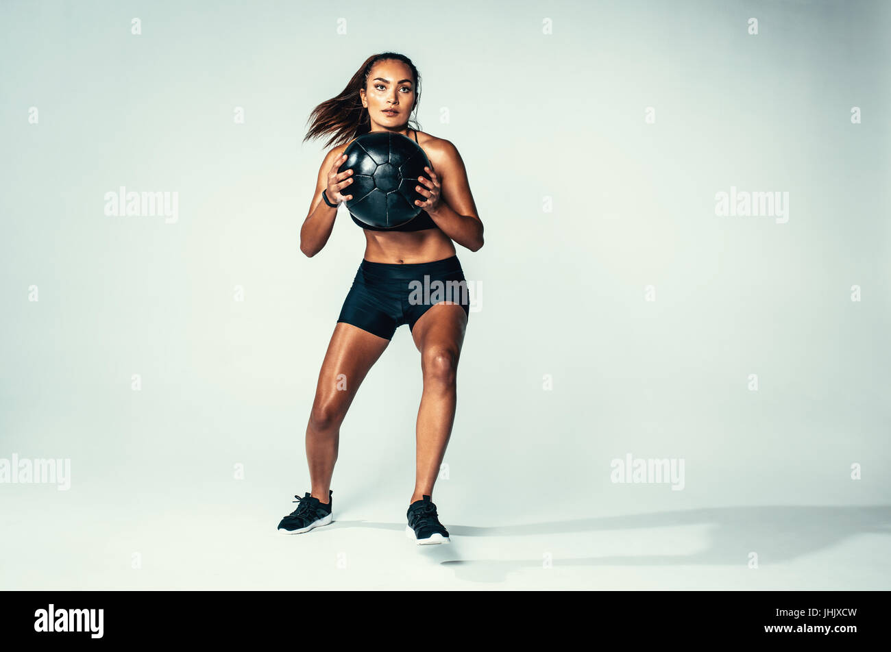 Studio shot of fit young woman with medicine ball. Female model with muscular body exercising with fitness ball over grey background. Stock Photo