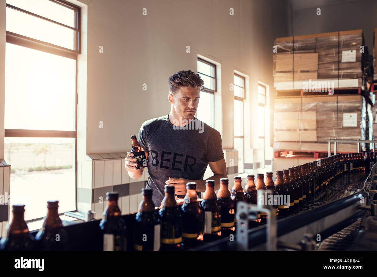 Young man working at small craft beer making factory and checking the quality of beer. Young businessman testing the beer bottle at brewery. Stock Photo