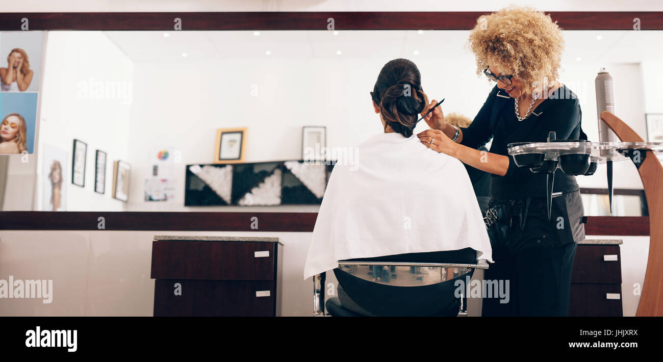 Hairdresser styling the hair of a customer at salon. Female hair stylist setting hair in fashionable design using a comb. Stock Photo