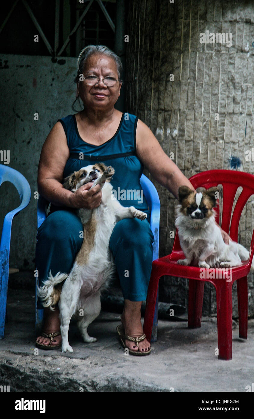 An elderly Vietnamese lady plays with her pet dogs in a street in Ho Chi Minh City, Vietnam Stock Photo
