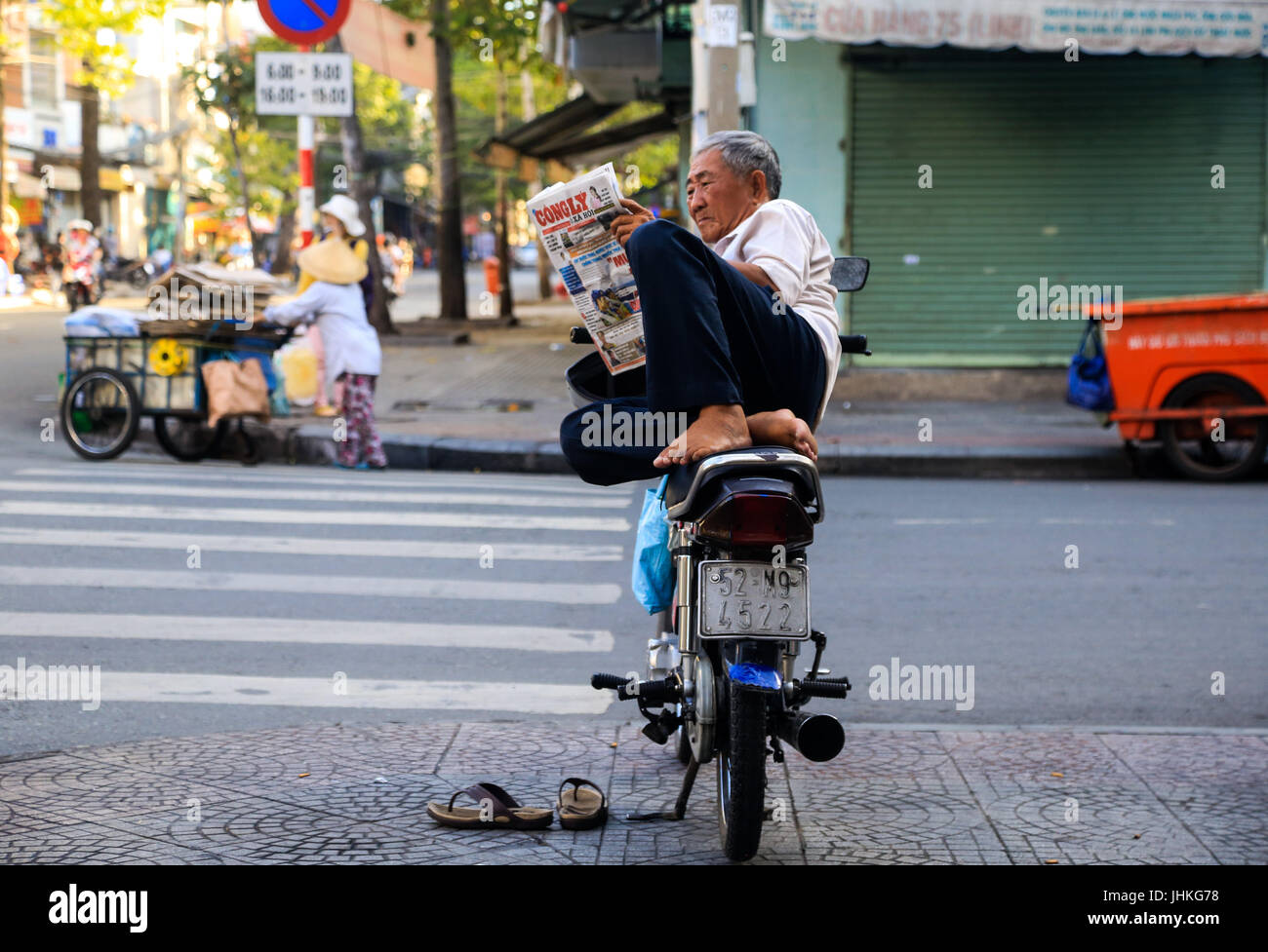 A Vietnamese motorbike taxi driver reads a newspaper whilst sitting on