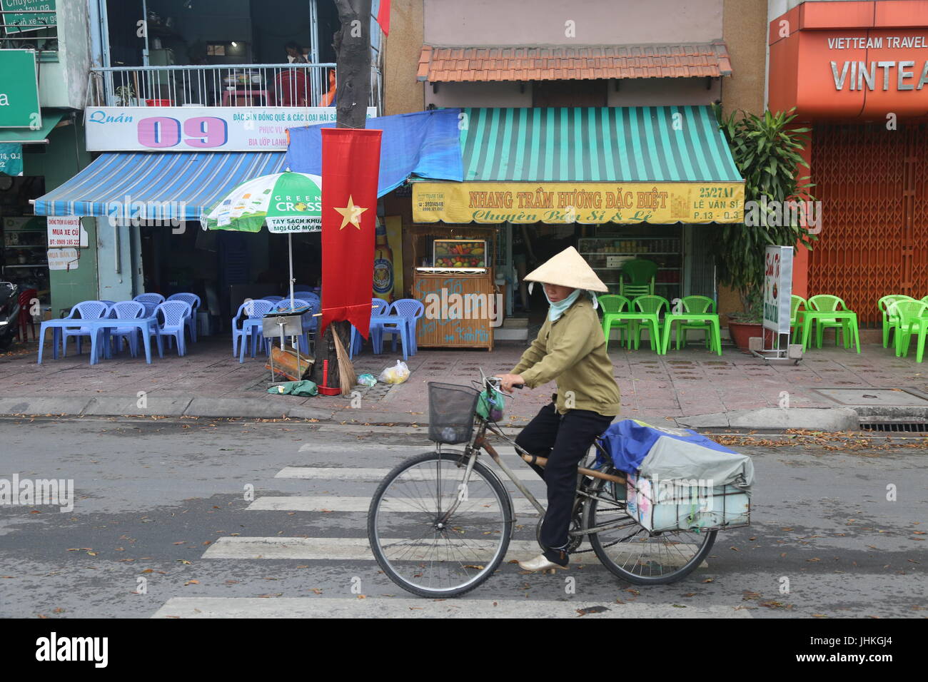 A  female Vietnamese street vendor rides a bike along a street Ho Chi Minh City, Vietnam Stock Photo
