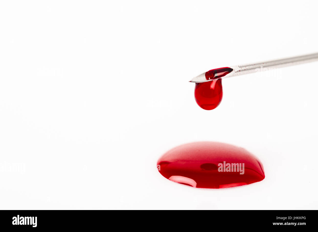 Macro view of drop of blood from needle syringe over white background. Stock Photo