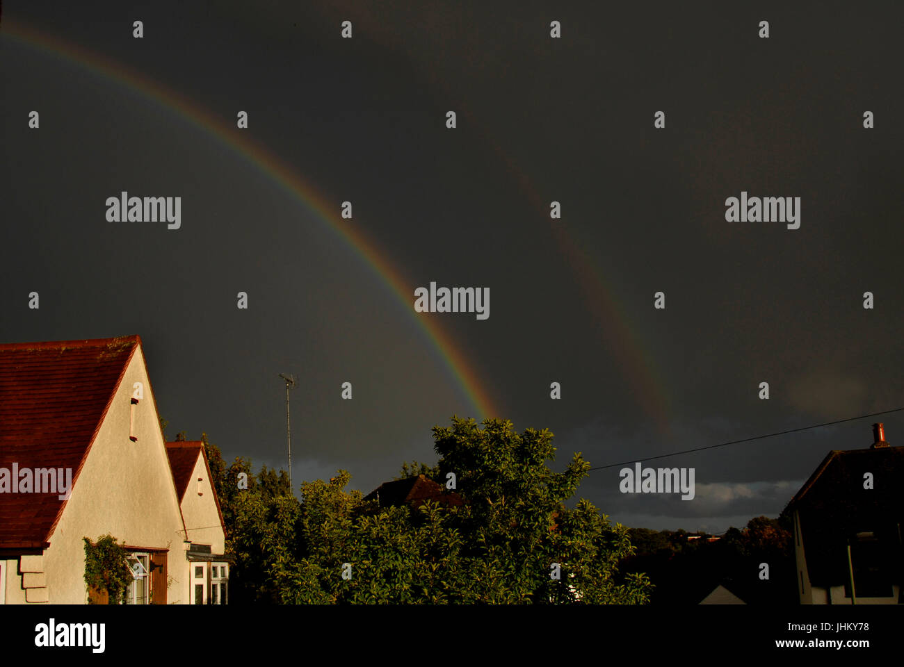 Double rainbow and dark clouds over suburban houses Stock Photo