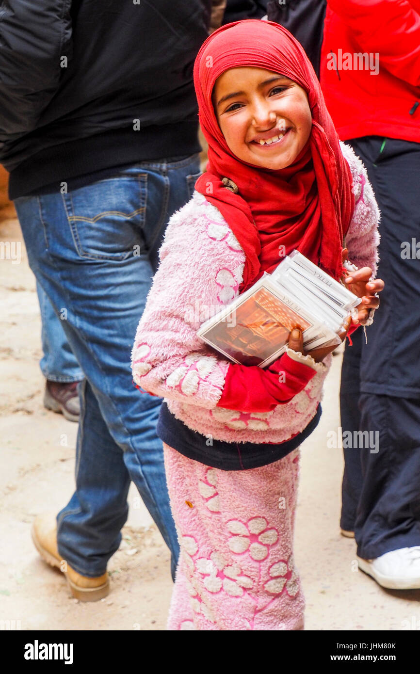 A young Bedouin girl wearing a red headscarf selling guidebooks to Petra, Jordan. Stock Photo