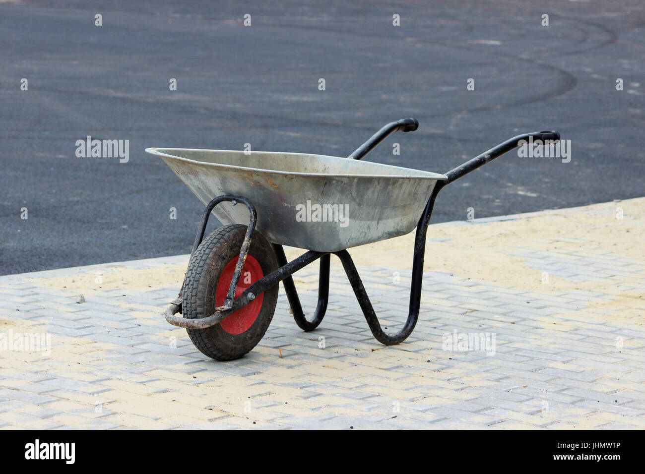 A construction empty wheelbarrow stands on the sidewalk next to an