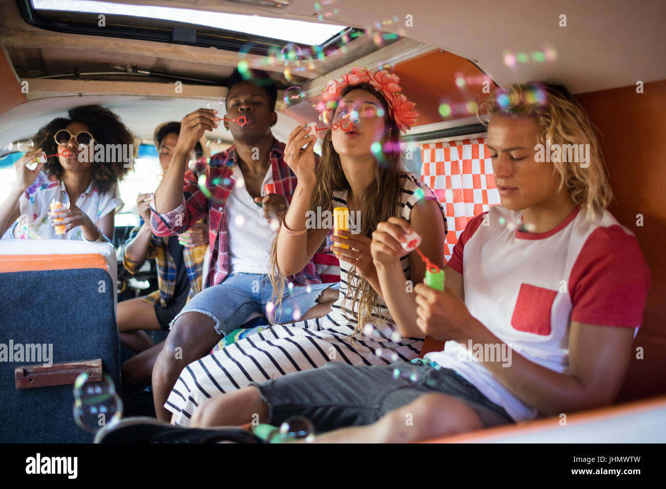 Young friends blowing bubble wands while sitting in camper van Stock Photo