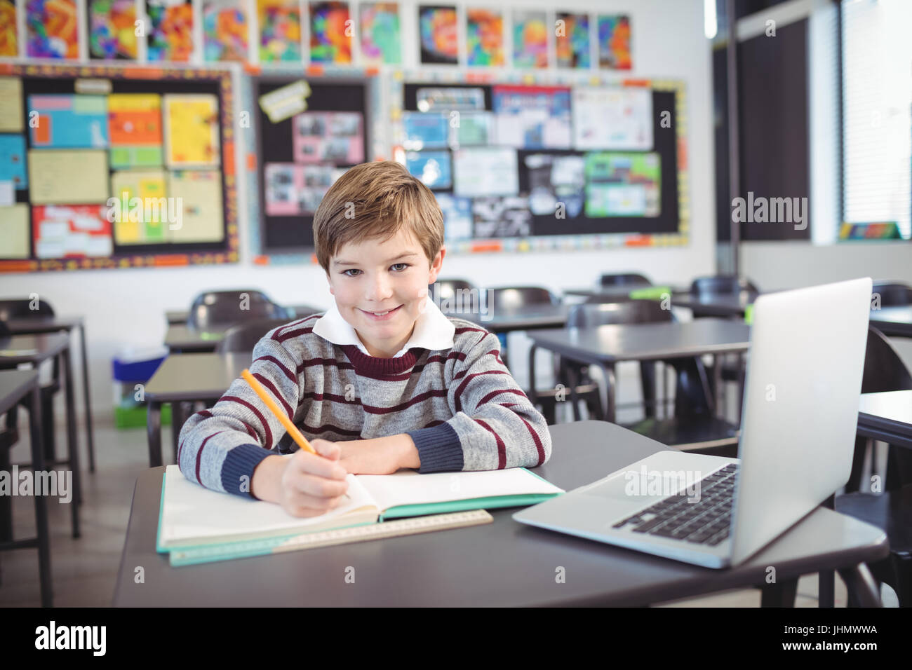 Portrait of smiling elementary schoolboy studying while sitting at desk ...