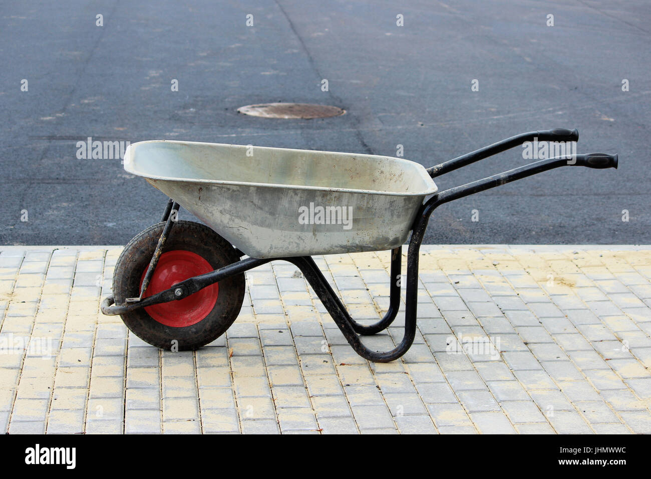 A construction empty wheelbarrow stands on the sidewalk next to an