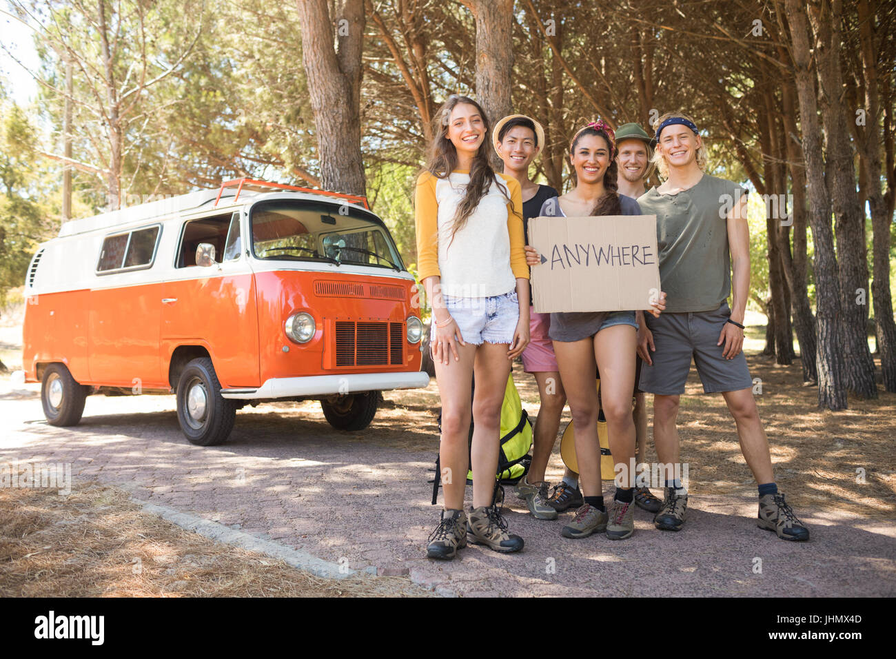 Portrait of smiling friends with sign board standing by camper van on field Stock Photo