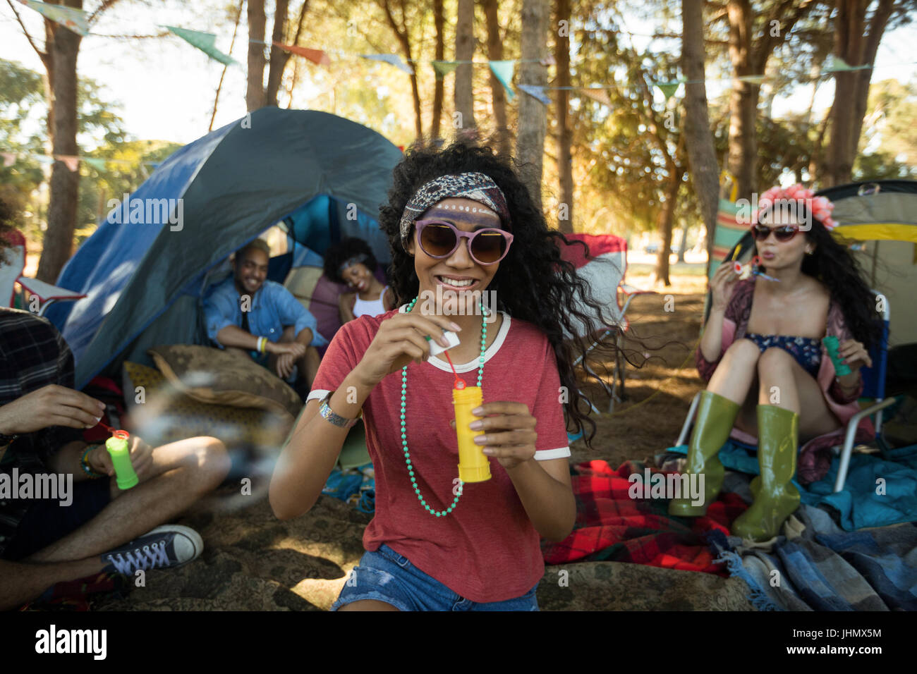 Smiling young woman holding bubble wand with friends in background at campsite Stock Photo