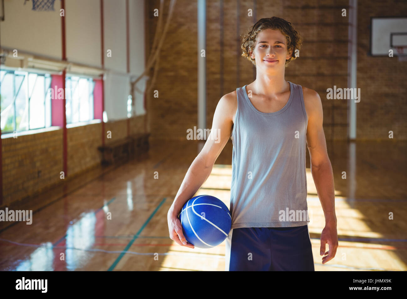 Portrait of smiling young man with basketball standing on hardwood floor in court Stock Photo