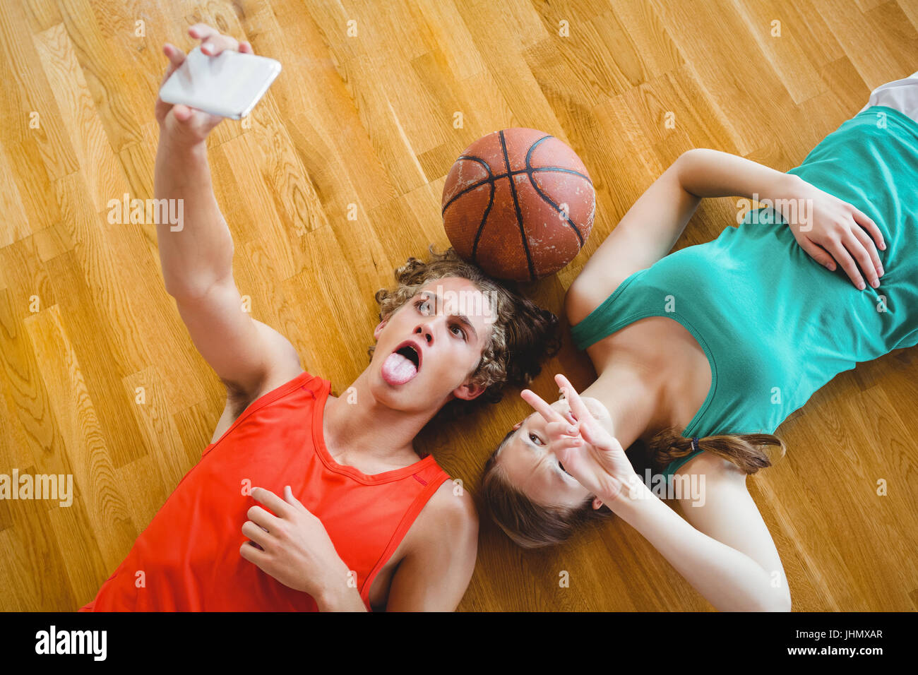 Overhead view of friends taking selfie while lying on hardwood floor in court Stock Photo