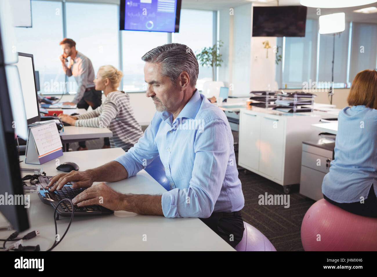 Businessman Working At Desk While Sitting On Exercise Ball In