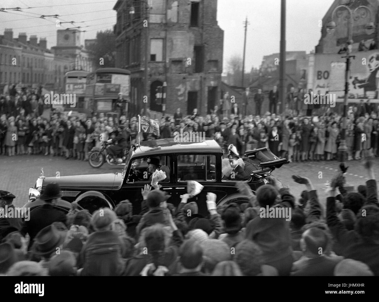 King George VI and Queen Elizabeth in an open car passing through the bond-damaged East End of London during their Stae drive in celebration of their Silver Wedding anniversary. Stock Photo