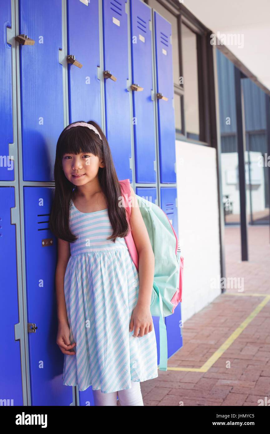 Portrait of elementary girl standing by lockers in corridor at school ...
