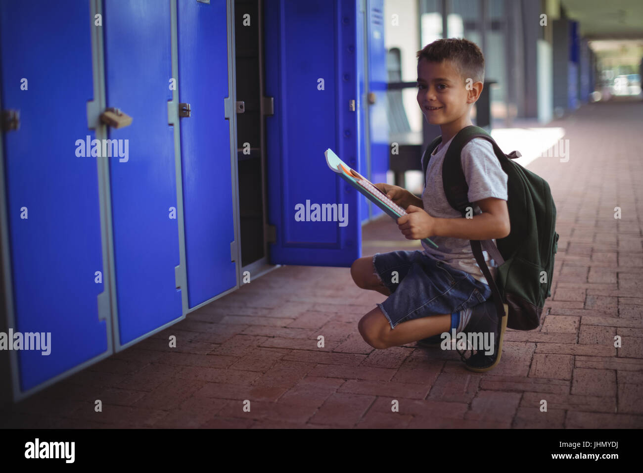 Portrait of boy holding books by open locker at school corridor Stock ...