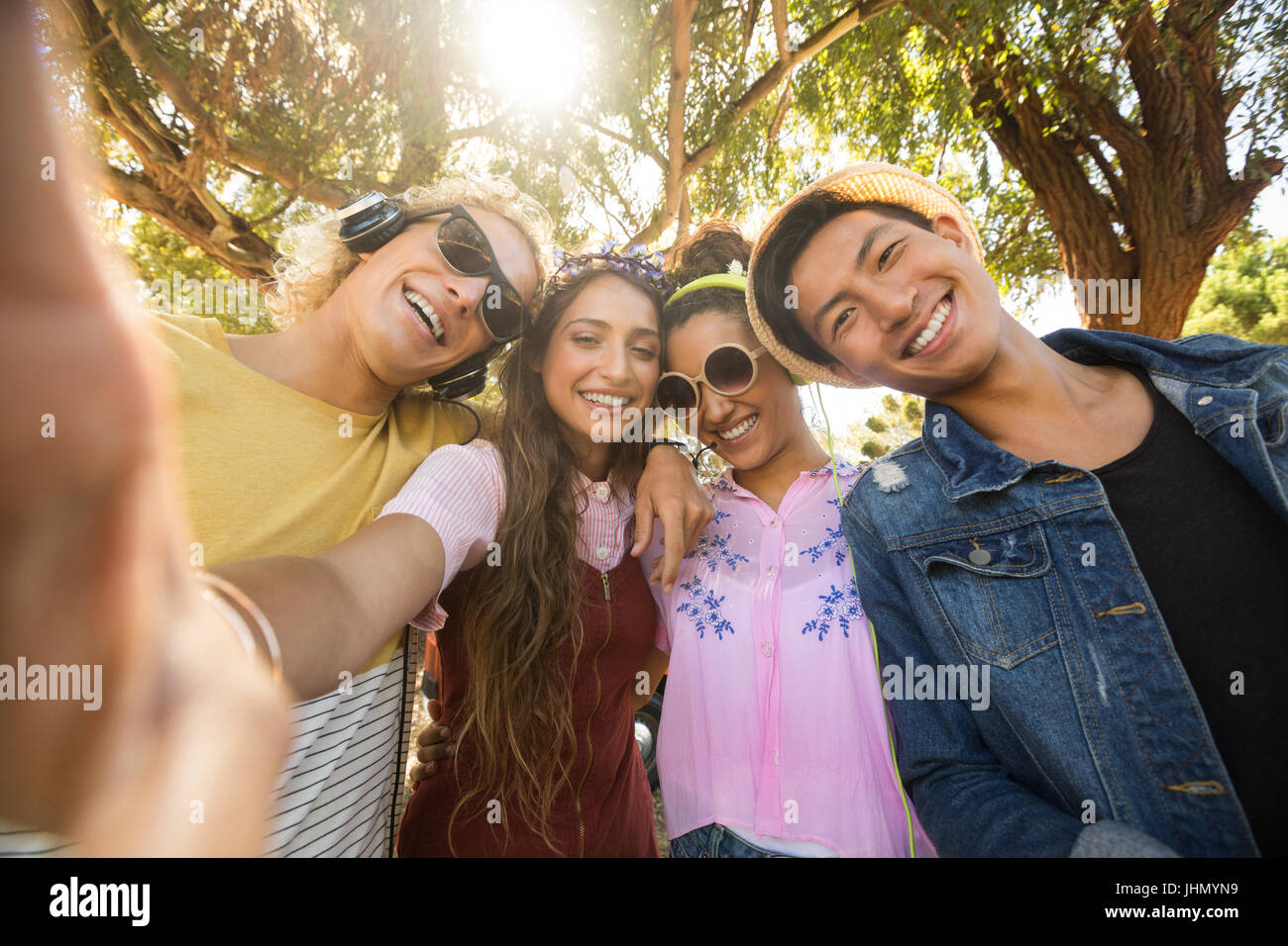 Portrait of smiling friends standing side by side against trees on sunny day Stock Photo