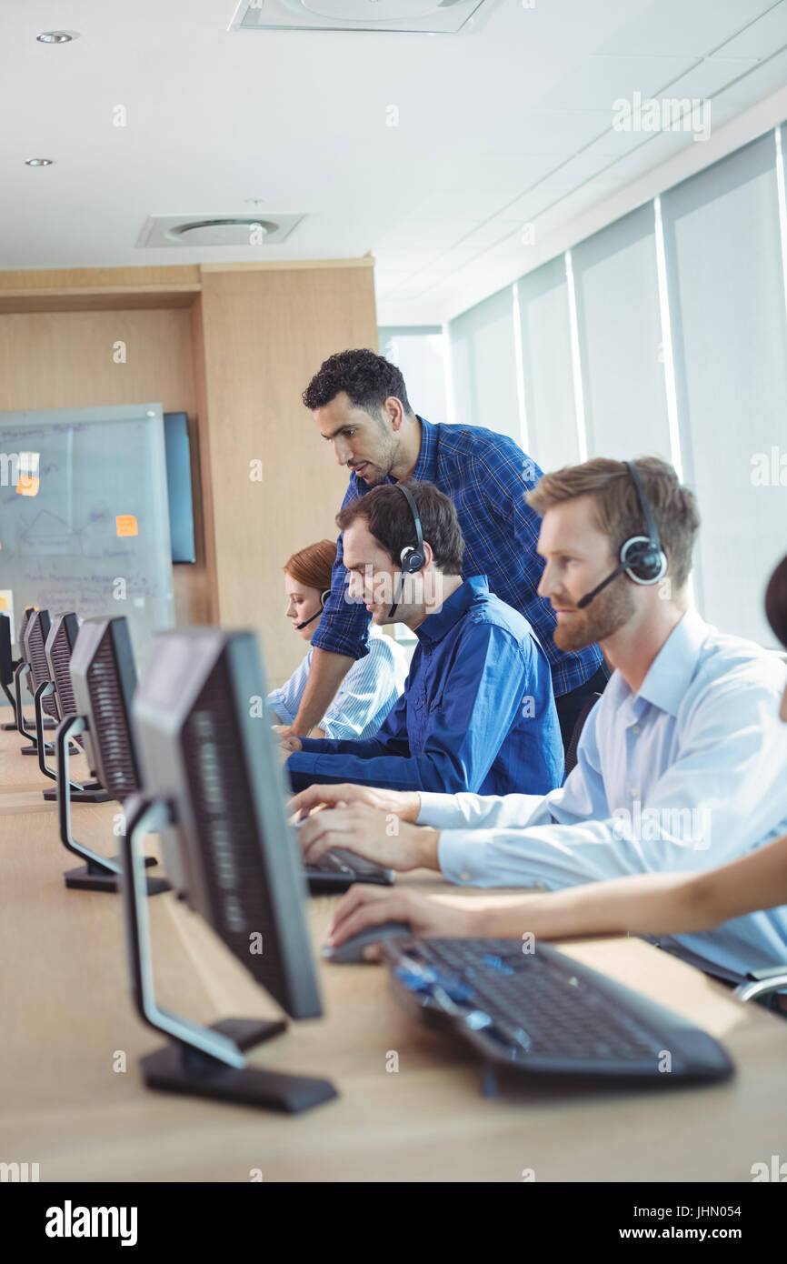 Male supervisor talking with telemarketer at desk in call center Stock