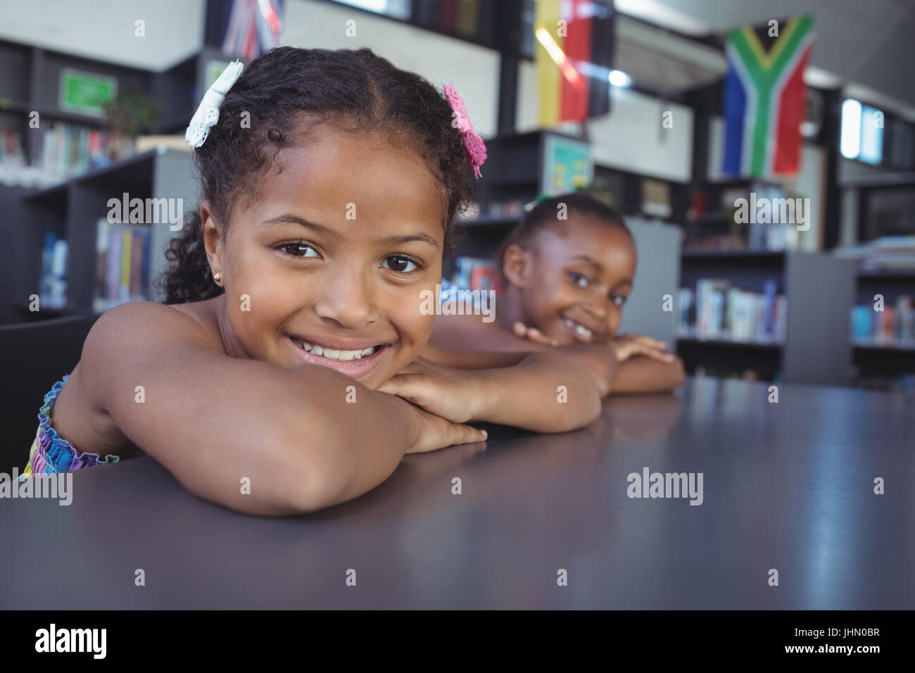 Close up portrait of smiling girls leaning on desk in library Stock ...