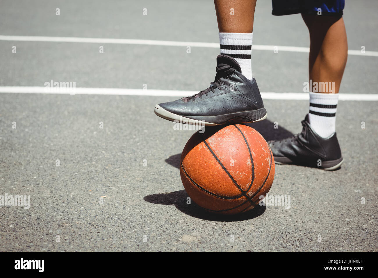 Low section of man standing with one leg on basketball at court Stock