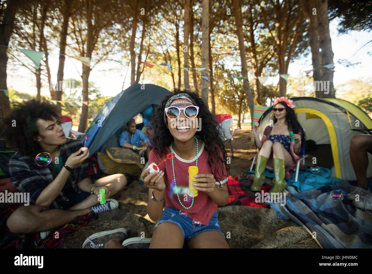 Happy young woman holding bubble wand with friends in background at campsite Stock Photo
