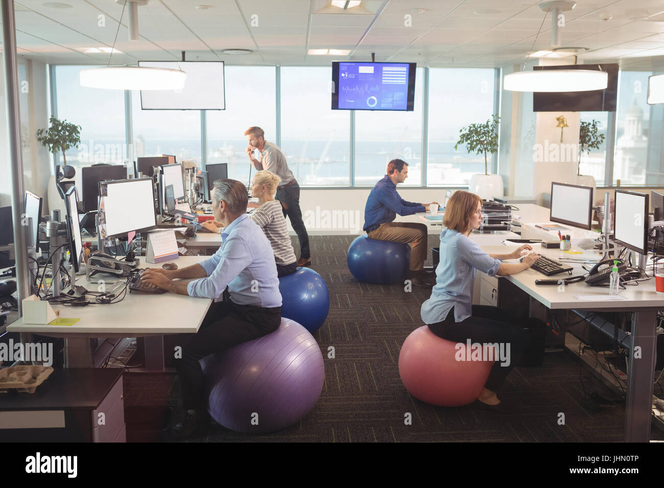 Business People Working At Desk While Sitting On Exercise Balls In