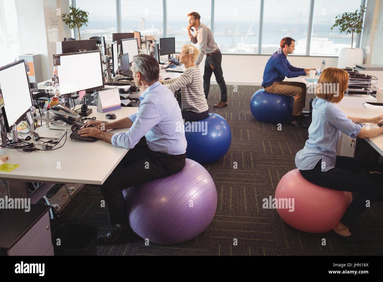 Business People Sitting On Exercise Balls While Working At Desk In