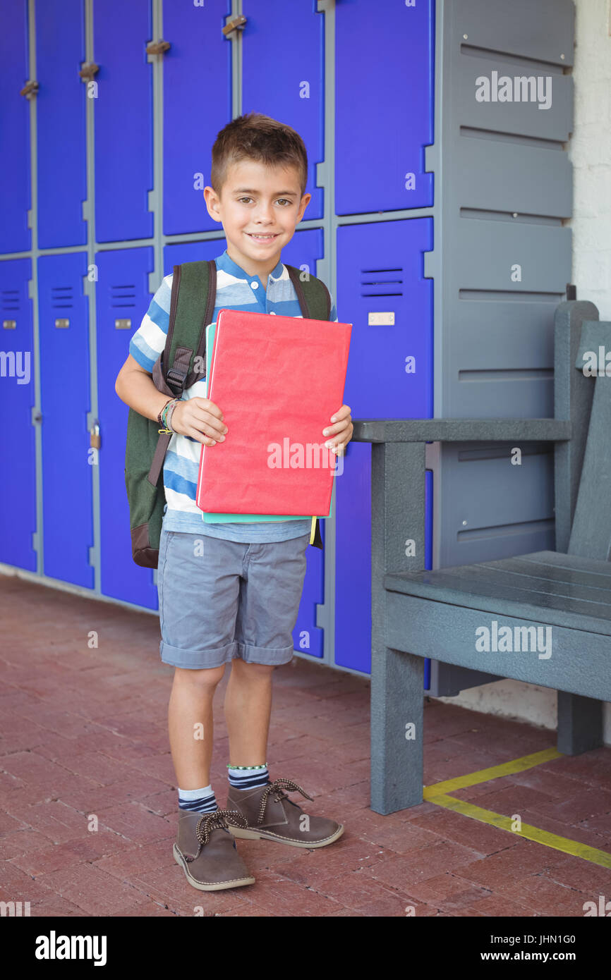 Portrait of happy boy holding books in corridor at school Stock Photo ...