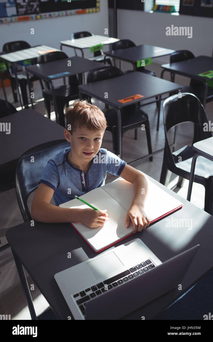 Portrait of smiling boy with laptop and book at desk in school Stock ...