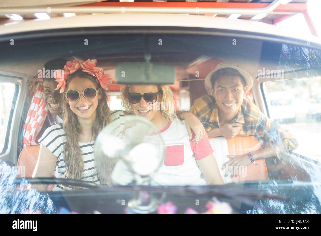 Portrait of happy friends sitting together in camper van seen through windshield Stock Photo