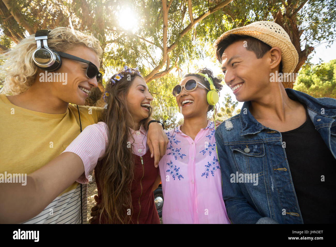 Close-up of smiling friends standing side by side against trees on sunny day Stock Photo