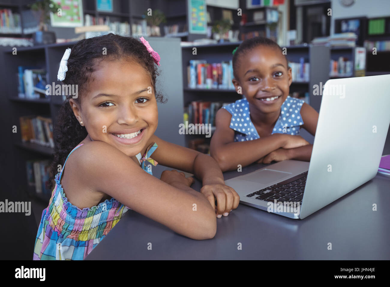 Portrait of smiling girls with laptop at desk in library Stock Photo ...