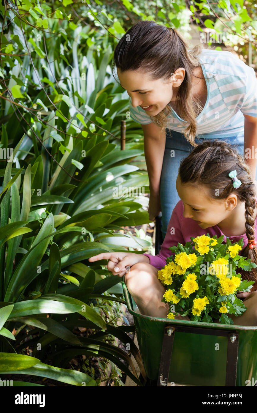 Mother looking while daughter sitting in wheelbarrow pointing towards ...