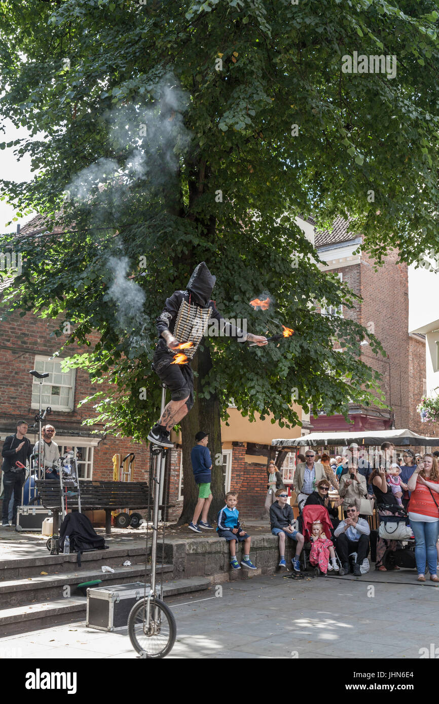 A hooded street entertainer on a unicycle and juggling burning torches in the city center in York,England,UK Stock Photo