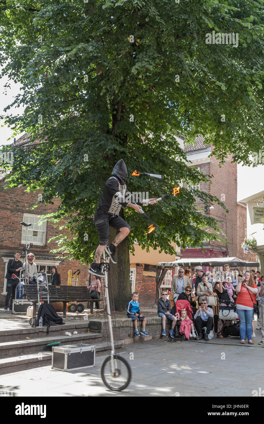 A hooded street entertainer on a unicycle and juggling burning torches in the city center in York,England,UK Stock Photo