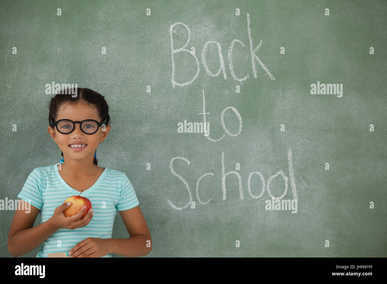Young girl in spectacles hat holding apple against chalk board Stock Photo