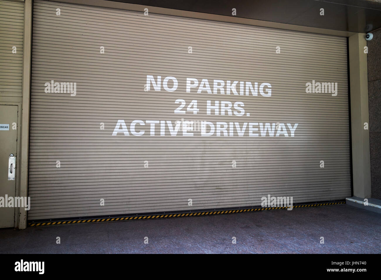 no parking 24 hrs active driveway sign on steel shutter entrance to underground parking midtown New York City USA Stock Photo