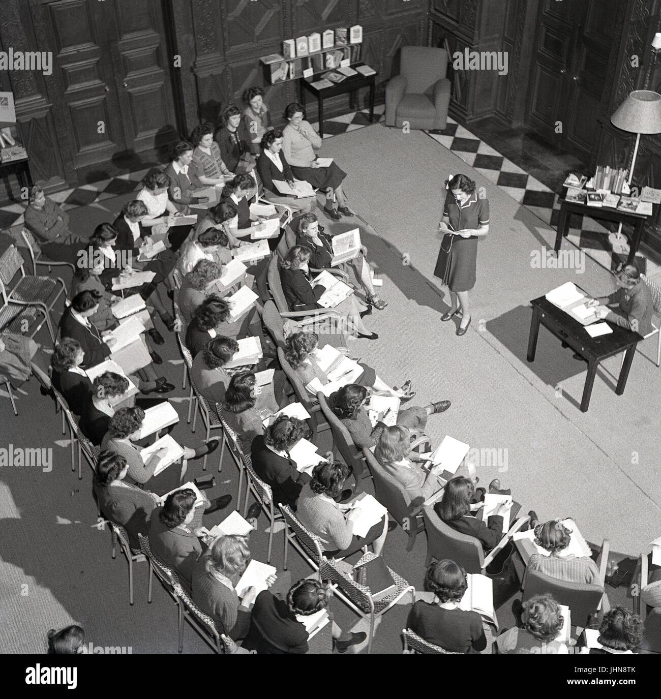 1950s, historical, England, womens teachers training college, overhead view of a young female presenting to her fellow students inside a hall. Stock Photo