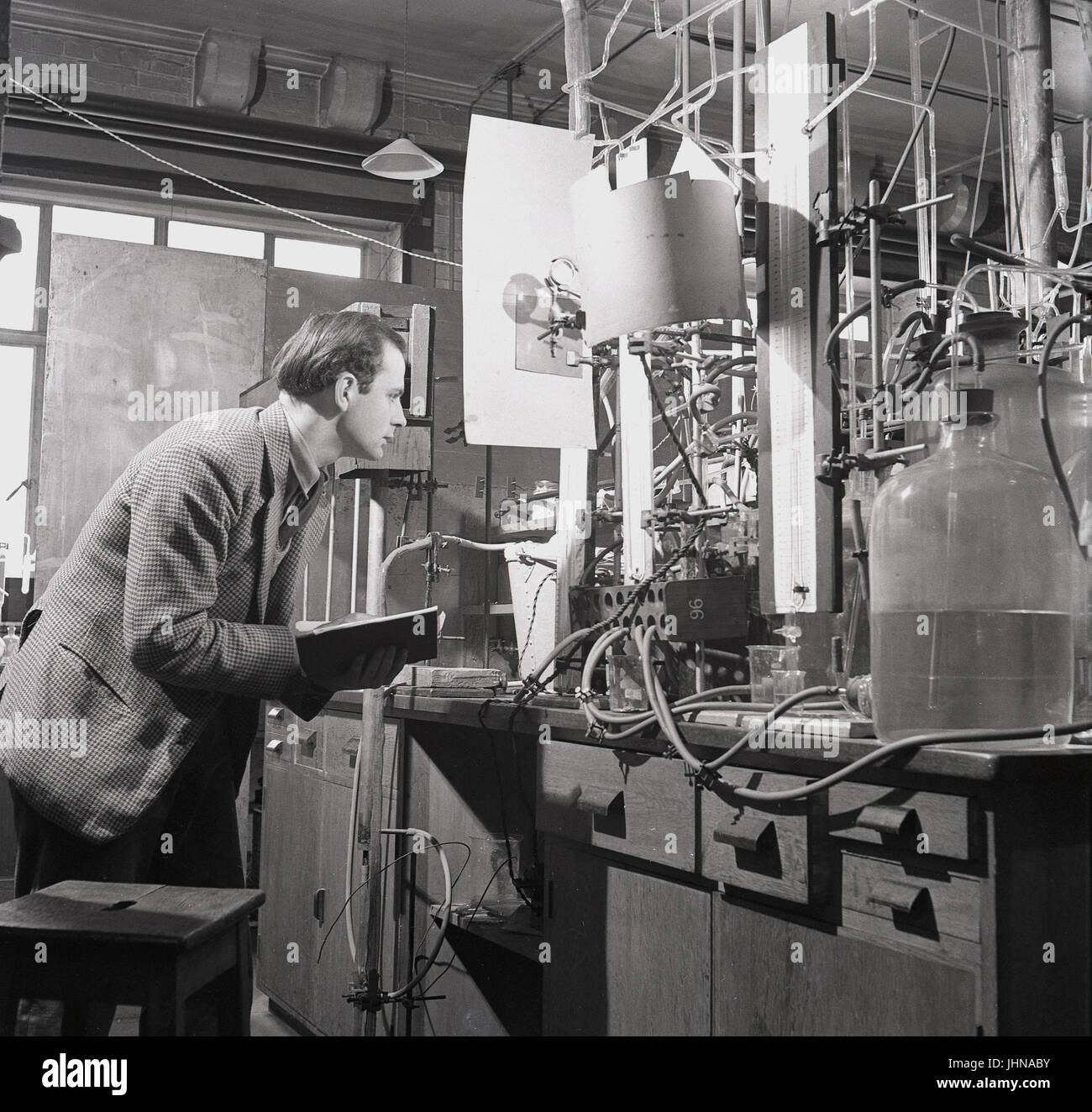 1950s, historical, male research scientist with notebook studies the results of the experiment using the flame propogation apparatus in the science laboratory at Oxford University, Oxford, England, UK. Stock Photo