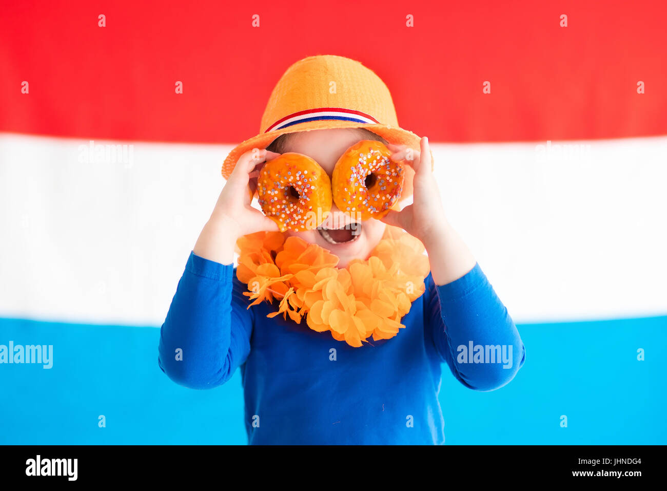 Little Dutch boy girl wearing country symbols eating orange donuts celebrating King day. Children support Holland sport team. Kids from the Netherland Stock Photo