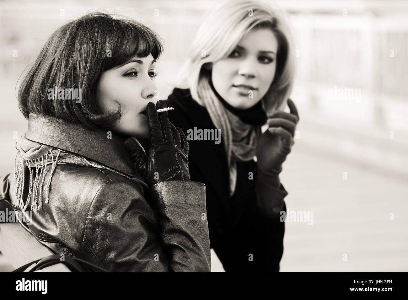 Two happy young fashion women smoking on the bench Stock Photo