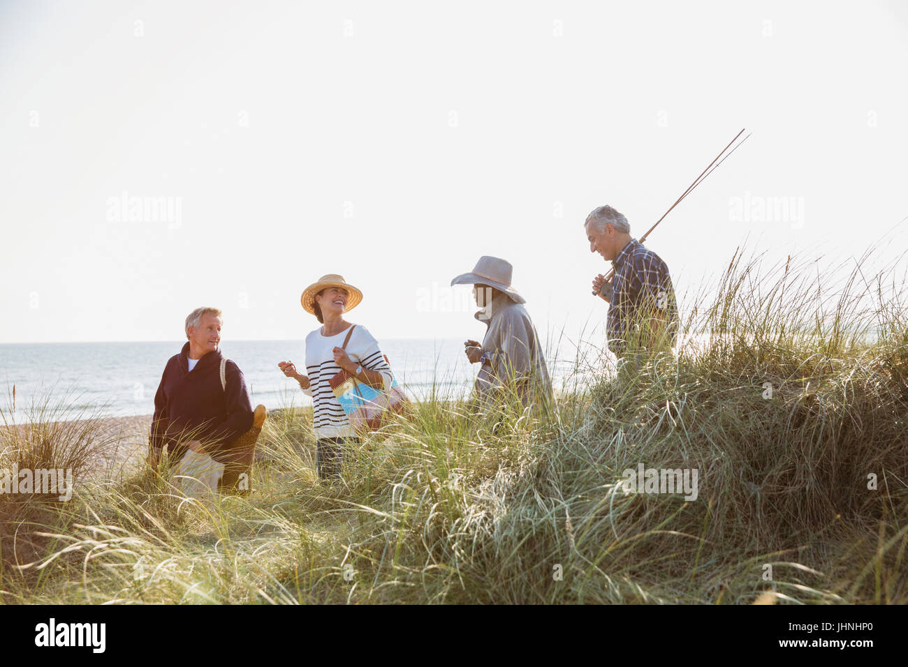 Senior couples with fishing pole walking in sunny beach grass Stock Photo