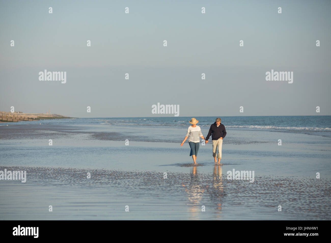 Mature couple holding hands walking in sunny ocean beach surf Stock Photo