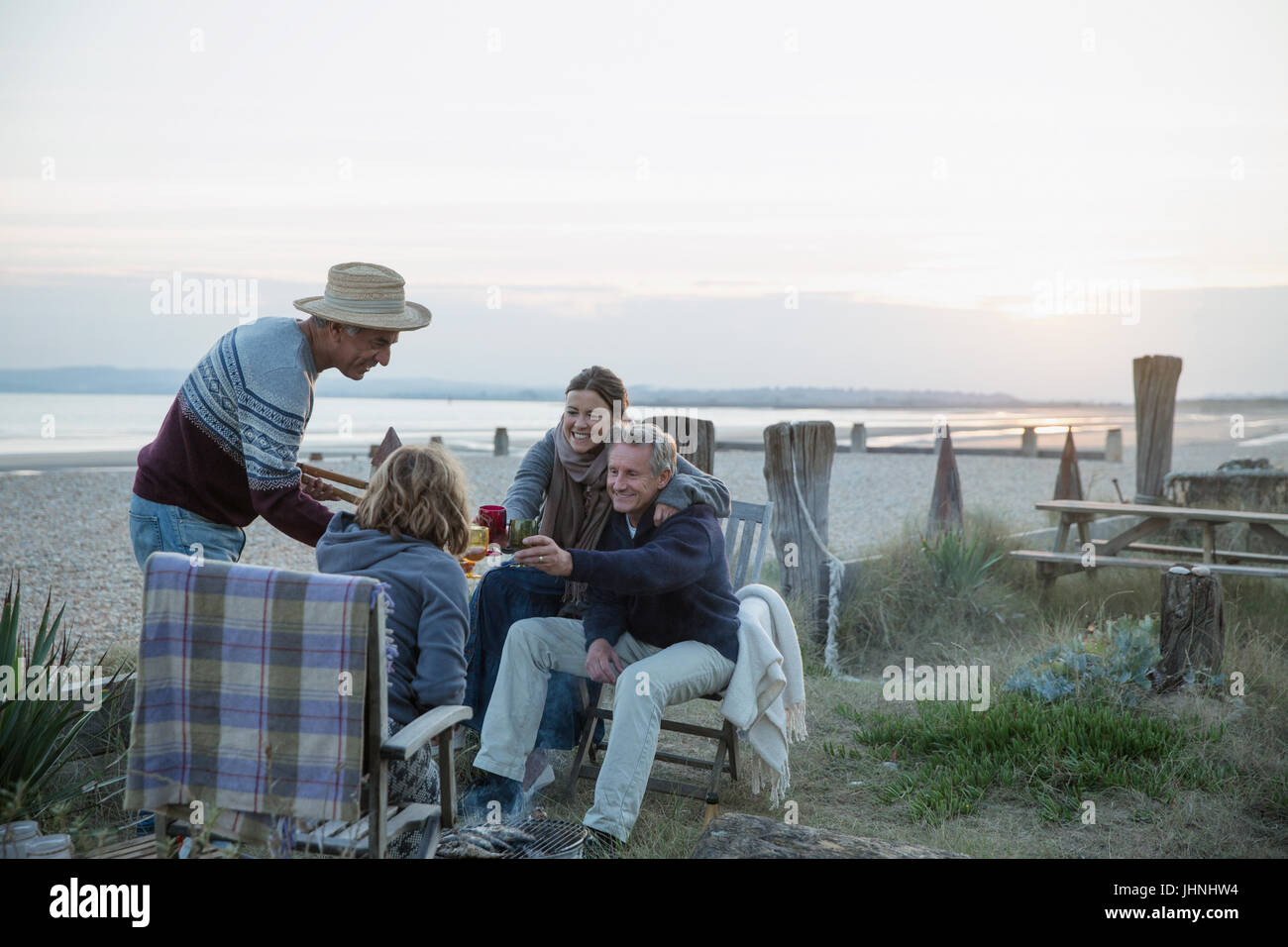 Mature couples barbecuing, drinking wine on sunset beach Stock Photo
