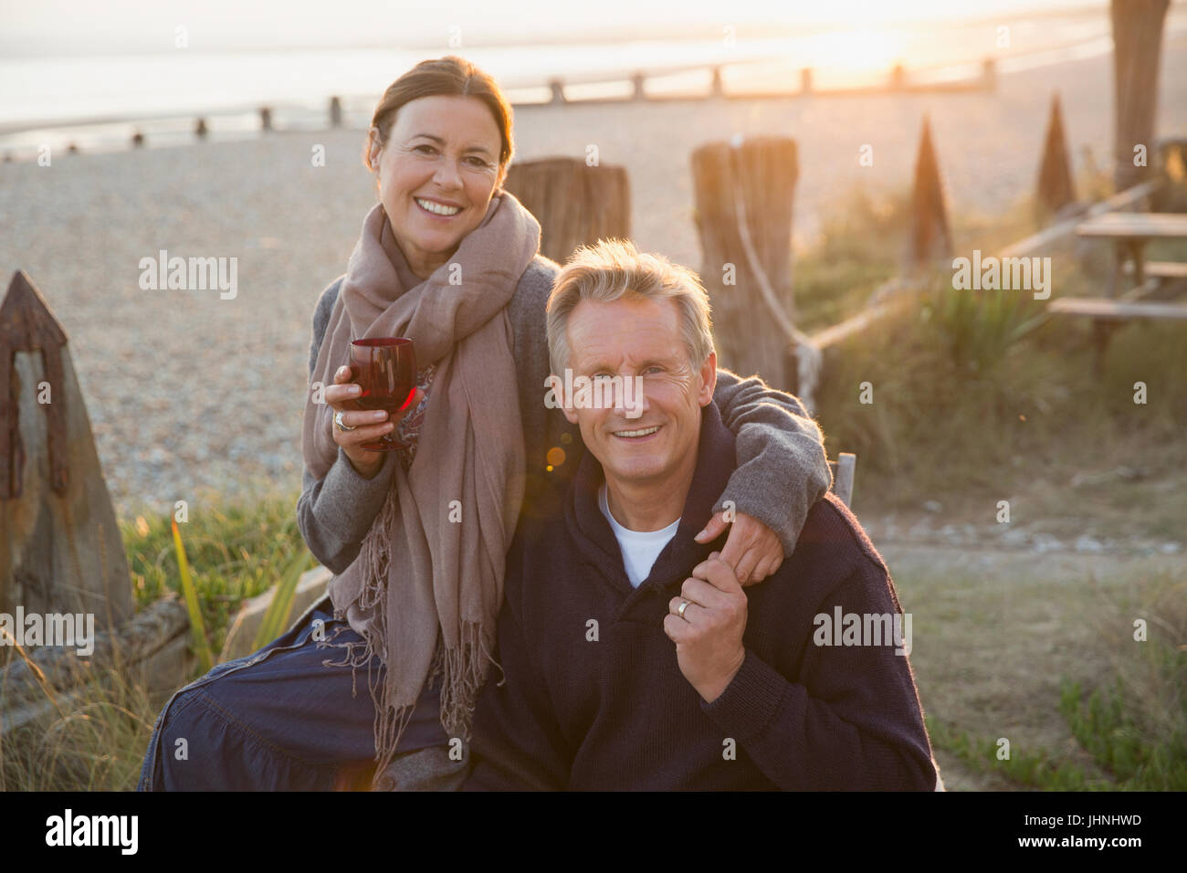 Portrait smiling mature couple holding hands and drinking wine on sunset beach Stock Photo