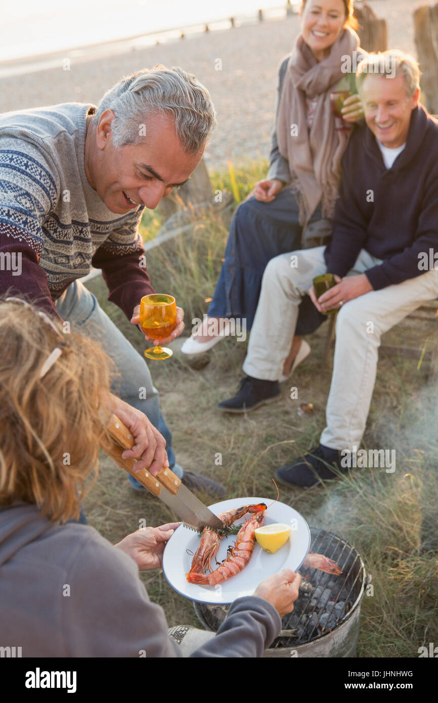 Mature couples barbecuing and drinking wine on beach Stock Photo